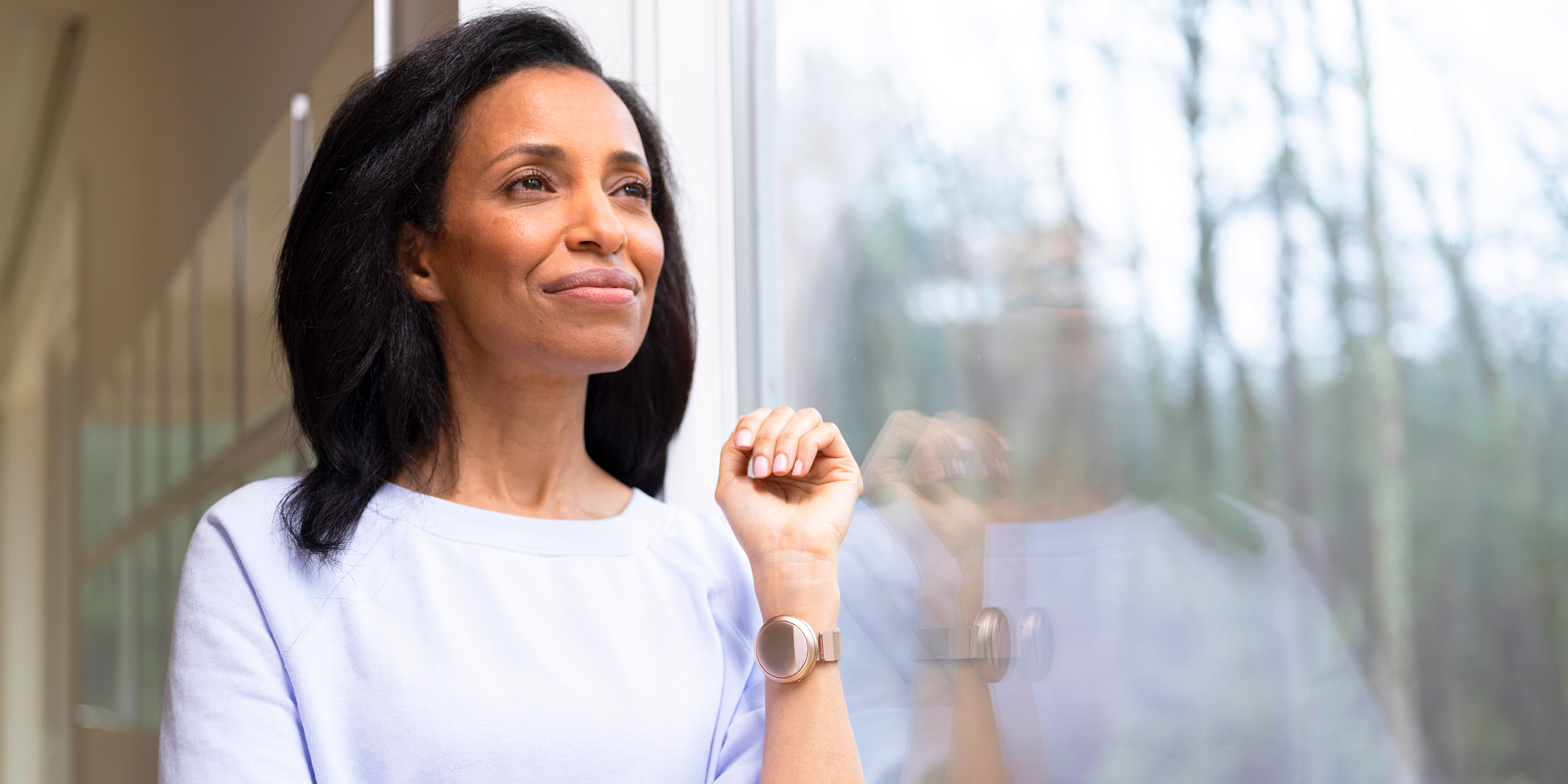 Smiling woman looking out the window wearing the rose gold Embr Wave 2 wristband..