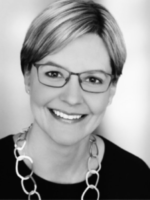 Black and white headshot of smiling woman with glasses.
