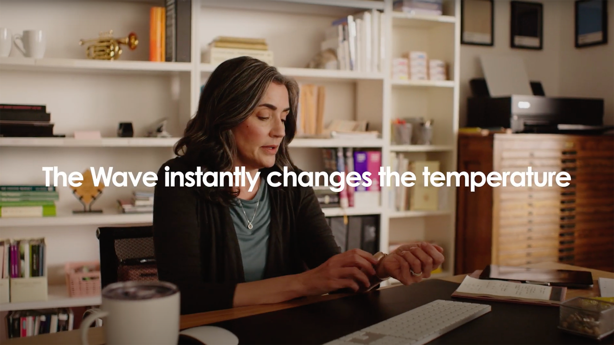 Woman at home office desk adjusting the rose gold Embr Wave 2 on her left wrist.