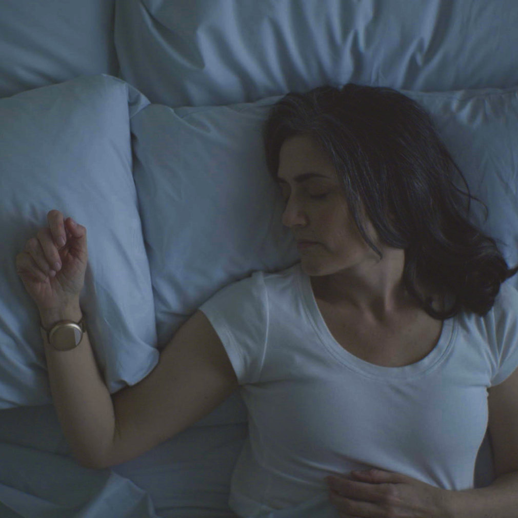 Sleeping woman in bed wearing the rose gold Embr Wave 2 bracelet on her right wrist.