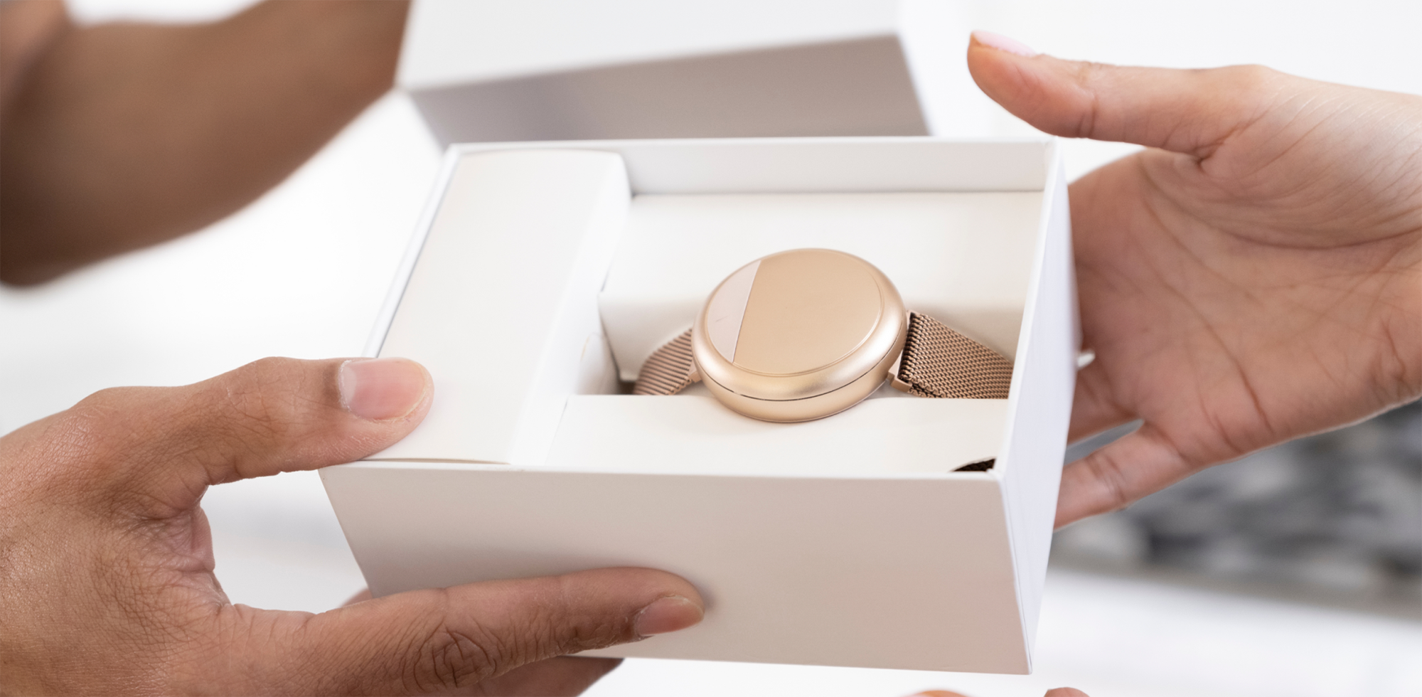 Hands holding the rose gold Embr Wave 2 bracelet in its white box.