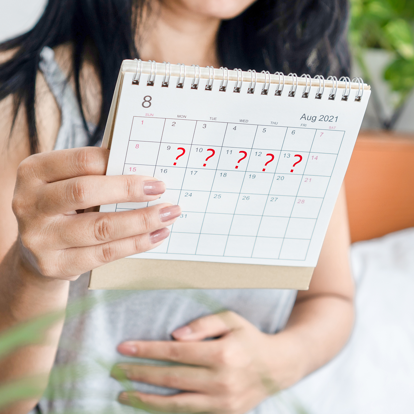 Woman with hand on belly holding desk calendar with red question marks on several days.