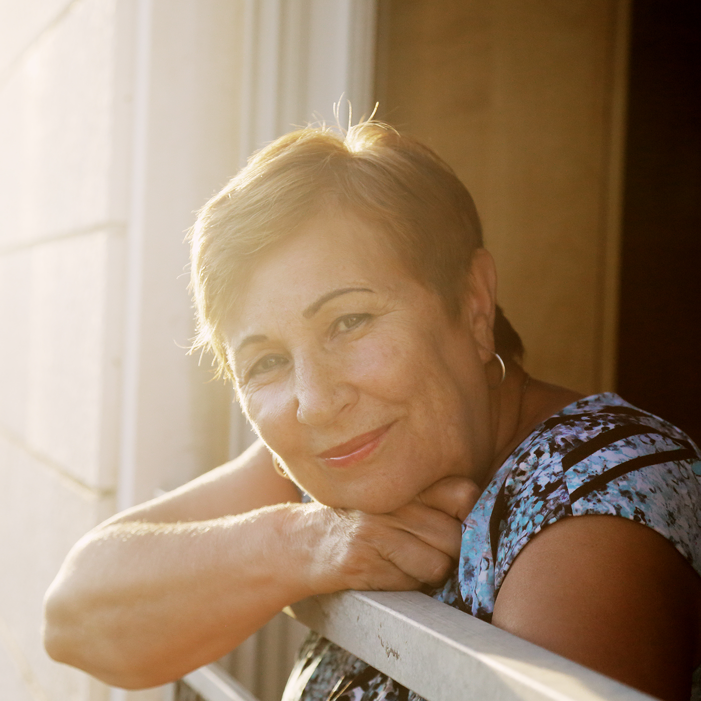 Woman smiling and leaning on patio railing with sun shining on her.